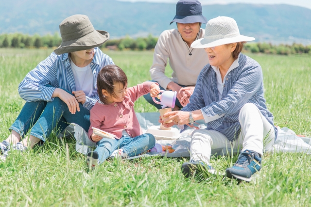 おばあちゃんのコップに子どもがお茶を注ぐ真似をしている様子を両親が微笑みながら見ている様子